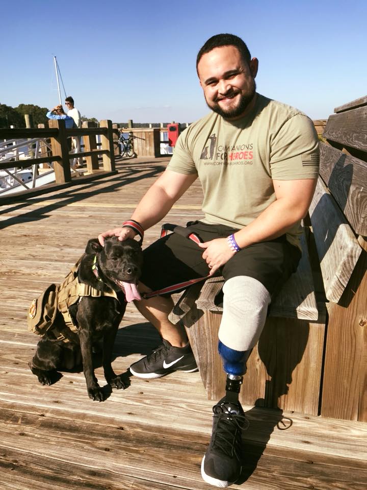 U.S. veteran with prosthetic left leg wearing Companions for Heroes t-shirt sits on dock bench with his dog